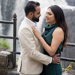 Pre-Wedding Photography in New Hyde Park, NY | The Glorious Memories A couple posing closely outdoors by a stone railing and waterfall, with the woman in a green dress and the man in a beige suit, during a pre-wedding photoshoot.