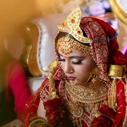 Traditional Indian Bride Photography by The Glorious Memories Traditional Indian bride in red and gold wedding attire with ornate jewelry and headpiece, captured in a close-up portrait by The Glorious Memories for bride photography in New Hyde Park, NY.